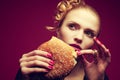 Unhealthy eating. Junk food concept. Portrait of fashionable young woman holding burger and posing over purple background. Close Royalty Free Stock Photo