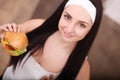 Unhealthy eating. Junk food concept. Portrait of fashionable young woman holding burger and posing over wood background. Close up. Royalty Free Stock Photo