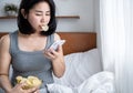 Asian woman with salty snack potato chips and using smart phone in bed