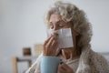Unhealthy elderly woman wiping runny nose with paper tissue.