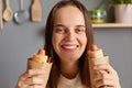Unhealthy food. Brown haired Caucasian young adult positive woman holding two hot dogs feels hungry, looking smiling at camera, Royalty Free Stock Photo
