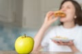 Unhealthy food choices. Wrong nutrition and overeating. Woman eats cheeseburger and fries against apple Royalty Free Stock Photo