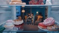 Unhealthy food on the shelves of an open refrigerator close up. Young couple sitting on the couch and eating, blurred Royalty Free Stock Photo