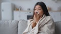 Unhealthy ill sick Asian woman multiethnic korean chinese girl patient covered in warm blanket at home blowing to paper Royalty Free Stock Photo