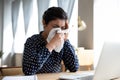 Unhealthy Indian woman blowing nose, sitting at workplace