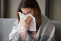 Unhealthy millennial girl covered in plaid using paper tissue.