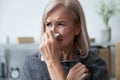 Unhealthy older woman covered in plaid, using paper tissue.