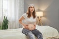 Unhealthy pregnant woman holding her belly while sitting on bed at home suffering from spasms starting contractions grimacing from Royalty Free Stock Photo