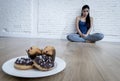 Unhealthy sugar donuts and muffins and tempted young woman or teenager girl sitting on ground