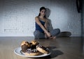 Unhealthy sugar donuts and muffins and tempted young woman or teenager girl sitting on ground