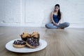 Unhealthy sugar donuts and muffins and tempted young woman or teenager girl sitting on ground
