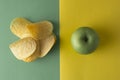 Unhealthy versus healthy food. Choise concept. Potatoe chips or green apple for snack. Top view, colorful background