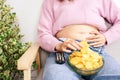 Unhealthy woman eating junk potato chips in bowl hand holding big, fat belly sitting on sofa watching tv