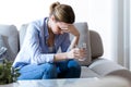 Unhealthy young woman with headache holding glass of water while sitting on sofa at home. Royalty Free Stock Photo