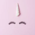 Unicorn face made of seashell with eyelashes on pastel pink background. Summer minimal concept