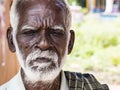 An unidentifed old senior indian poor man portrait with a dark brown wrinkled face and white hair and a white beard, looks serious