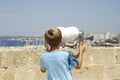 Unidentifiable blond child looks through the binoculars at the sea from Gallipoli castle. Apulia, Italy