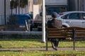 Unidentifiable lonely old man sitting on a park bench smoking a pipe