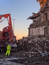 unidentifiable man in high visibility clothing working in front of an orange excavator on the demolition site of a large building Royalty Free Stock Photo