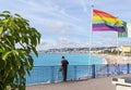 An unidentifiable man stands near a rainbow flag and looks over the Bay of Angels on the French Riviera, in Nice, France Royalty Free Stock Photo