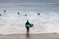 An unidentifiable man in a wetsuit carrying his surfboard getting ready to join other surfers already paddling out to catch waves Royalty Free Stock Photo