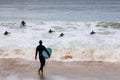 An unidentifiable man in a wetsuit carrying his surfboard getting ready to join other surfers already paddling out to catch waves Royalty Free Stock Photo