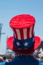 Unidentifiable person wearing American Flag red white and blue top hat. There is a blue sky in the background.