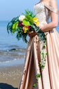 Unidentified bride in beautiful wedding dress holding gentle nice bridal bouquet with fresh blooming flowers, outdoors