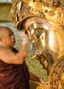 Unidentified Burmese monk is cleaning Buddha statue with the golden paper at Mahamuni Buddha temple, August