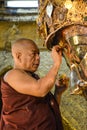 Unidentified Burmese monk is cleaning Buddha statue with the golden paper at Mahamuni Buddha temple, August