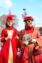 An unidentified couple of women dress elaborate red fancy dresses with masks, white gloves, jewels and hats with red feather durin