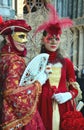 An unidentified couple of women dress elaborate red fancy dresses with masks, white gloves, jewels and hats with red feather