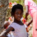 Unidentified Diola girl with braids in striped shirt stands in