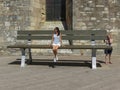 Unidentified elegant lady in summer clothes seated on a huge bench