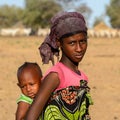 Unidentified Fulani girl in colored clothes and headscarf carri