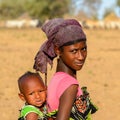 Unidentified Fulani girl in headscarf carries a baby on her bac