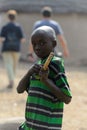 Unidentified Ghanaian boy in striped shirt holds a wooden objec