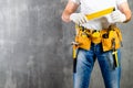 unidentified handyman standing with a tool belt with construction tools and holding a ruler against grey background. DIY tools