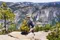 Unidentified hiker sitting on a rock and looking towards Yosemite Valley and Upper Yosemite Falls, Yosemite National Park,