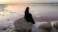 Unidentified Iranian woman in hijab burka sitting on a rock by the Maharloo pink lake, Shiraz, Iran