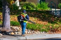 Unidentified landscape worker with a handheld backpack leaf blower clear fallen autumn leaves in an urban neighborhood. Yellow Royalty Free Stock Photo