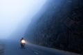 An unidentified male riding motorcycle on the dark misty mountain road, mystic asphalt road in mountain gorge