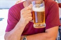 An unidentified man drinks out of a large glass mug of light beer on the background of a pub on a wooden table Royalty Free Stock Photo