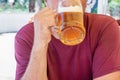 An unidentified man drinks out of a large glass mug of light beer on the background of a pub on a wooden table Royalty Free Stock Photo