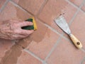 Unidentified man, workman, sponging down repaired grout between outdoor terracotta style patio tiles. Closeup detail.