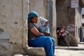 An unidentified Nepalese woman with a small child on her knees sits against the wall of a house on Jomsoma Street. Nepal