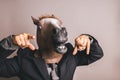 Unidentified person with a dark grey suit and tie wearing a horse mask pointing at the camera Royalty Free Stock Photo