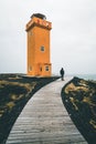 Unidentified Person standing in front of Orange Lighthouse Svortuloft Skalasnagi tower in Snaefellsnes Peninsula, west