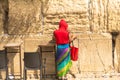 Unidentified tourist in a bright red jacket and colorful female scarf , harboring legs in shorts at the Western Wall