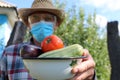 An unidentified unfocused person in a protective medical mask and goggles shows the harvest of vegetables.